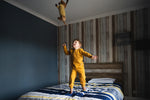 3 year old boy in turmeric pyjamas jumping bed throwing toy sausage dog in air