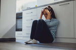 young millennial mother slumped kitchen floor hands on head distressed